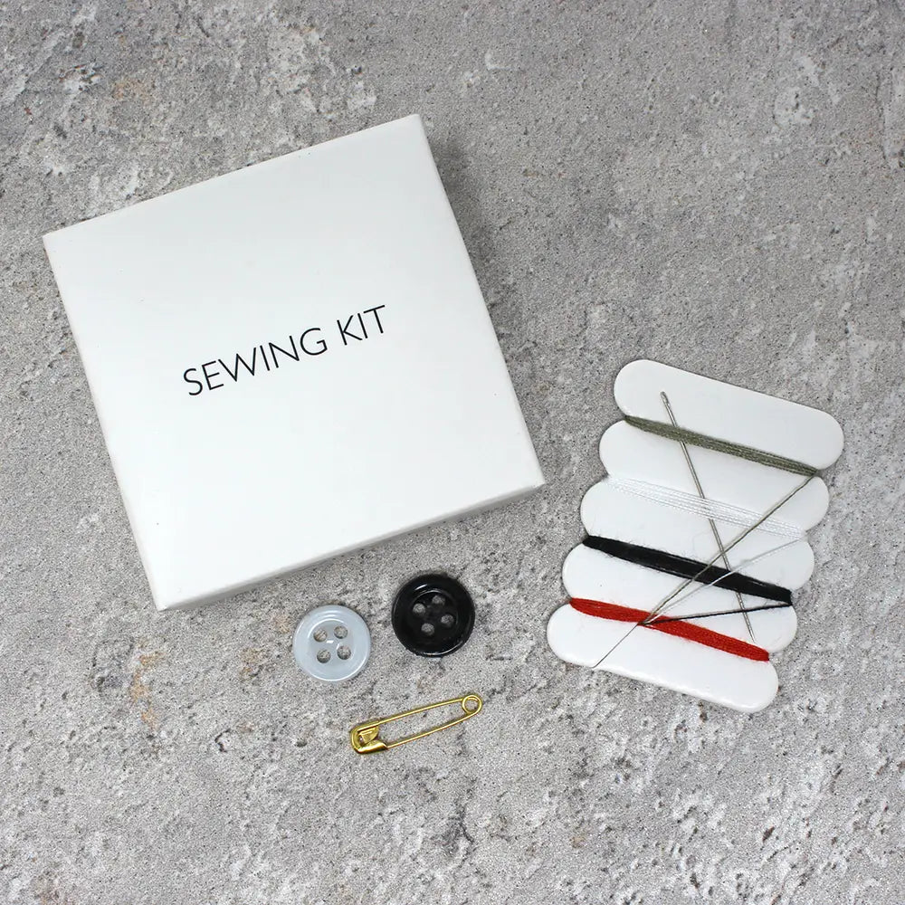 Sewing kit with box, pins, needle, thread, and buttons on a gray surface