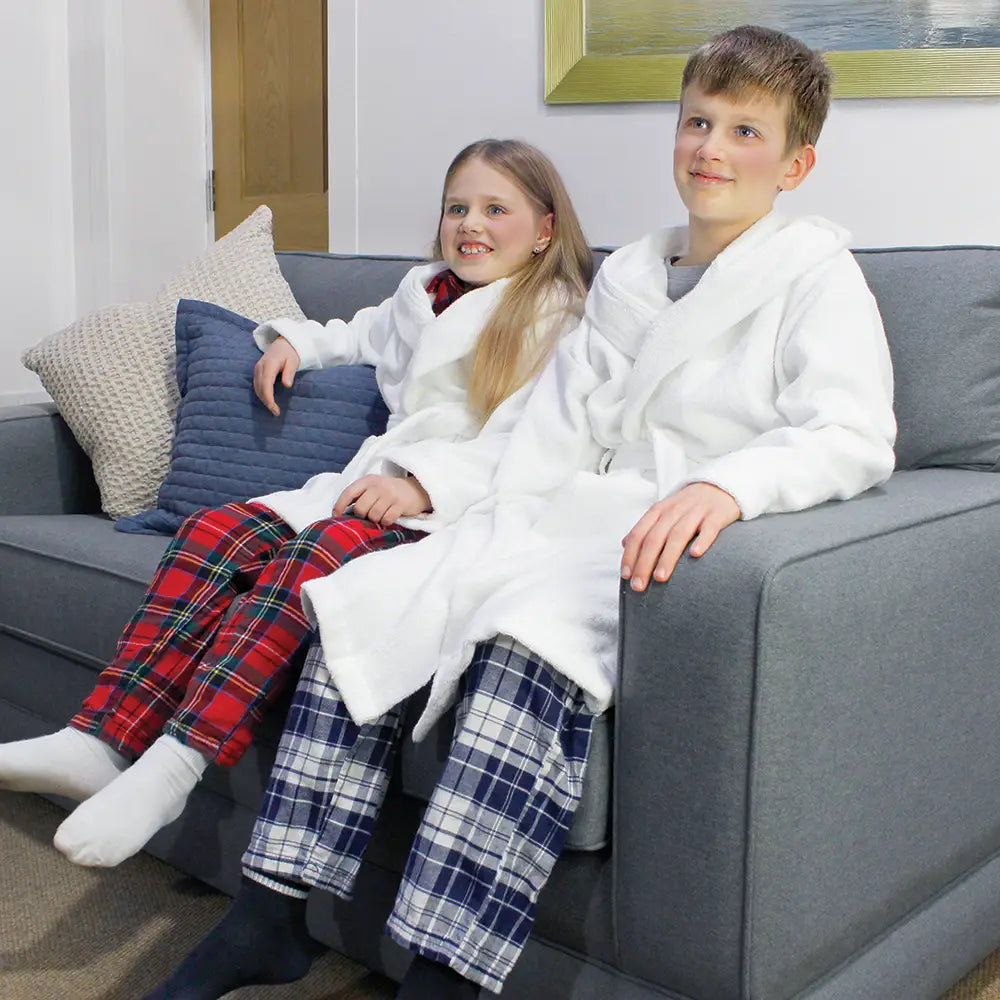 Two children in white robes and plaid pants sitting on a gray couch.