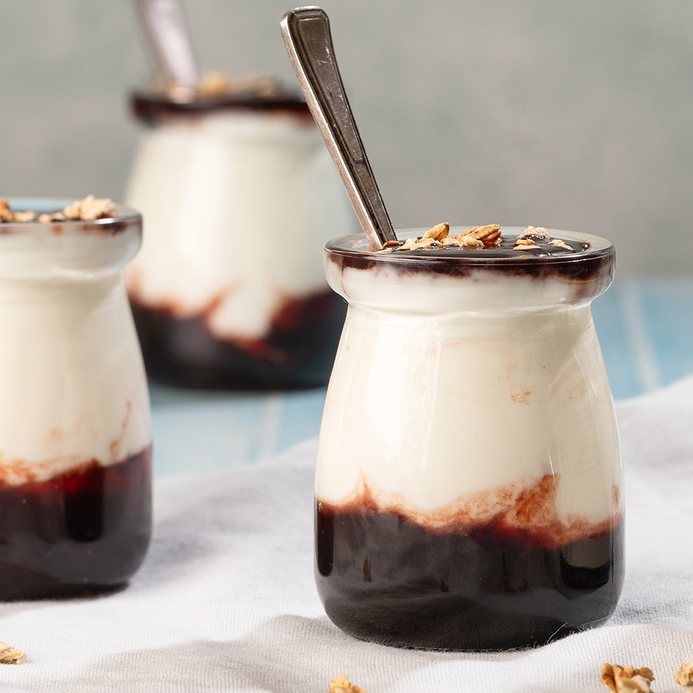 Three small glass jars filled with jam and yoghurt layered on a textured surface.