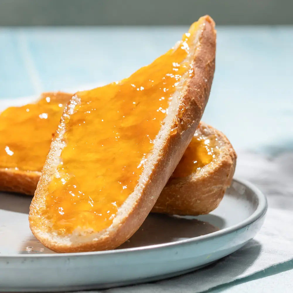 Two slices of bread with orange jam on a white plate against a light blue background