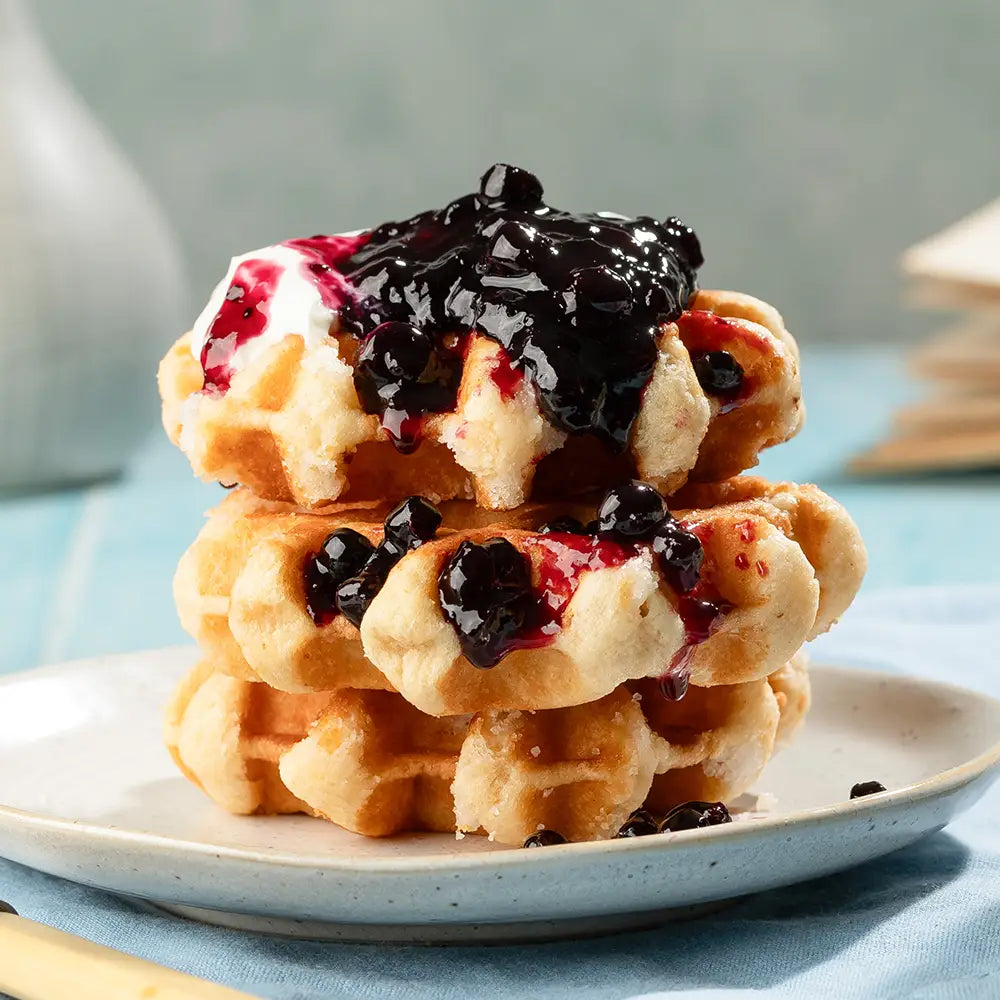 Stack of waffles with jam on a plate against a light blue background