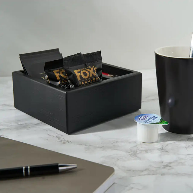 Black container with Fox Fabuloso packets on a marble surface with a coffee cup and notebook.