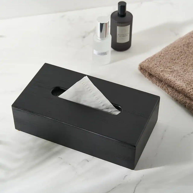 Black tissue box on a marble surface with a bottle and towel in the background