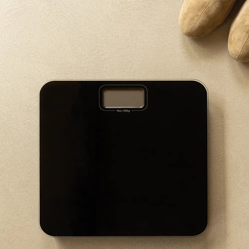 Black digital bathroom scale on a beige surface with a pair of brown shoes in the background.