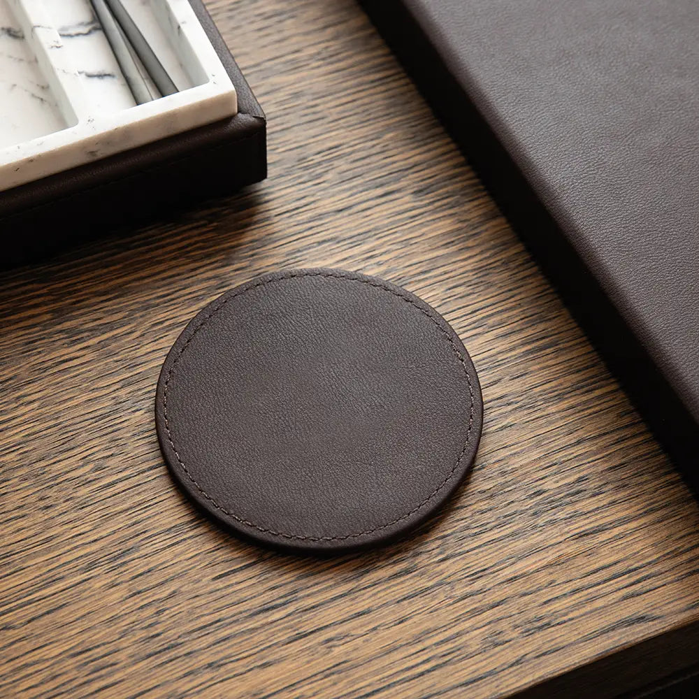 Round dark brown leather-effect coaster on a wooden surface