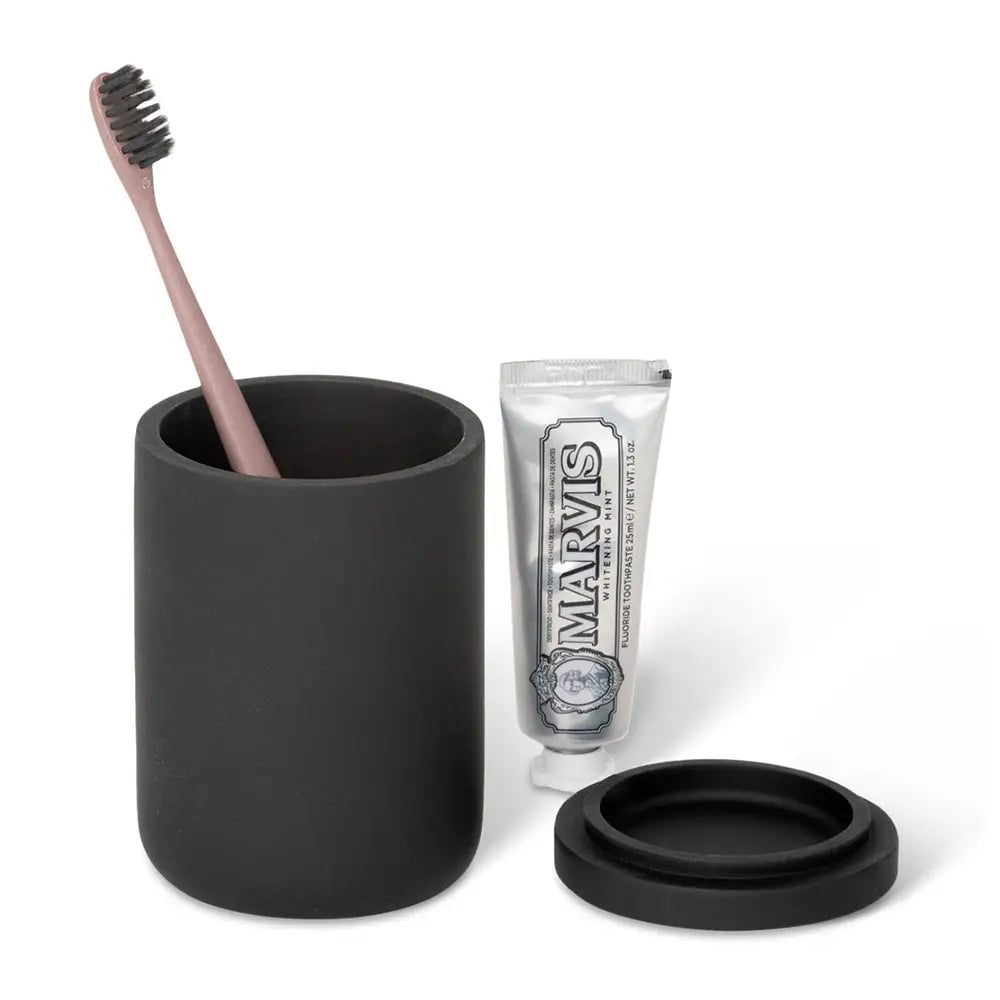 Black amenity jar with a toothbrush, black lid, and toothpaste on a white background