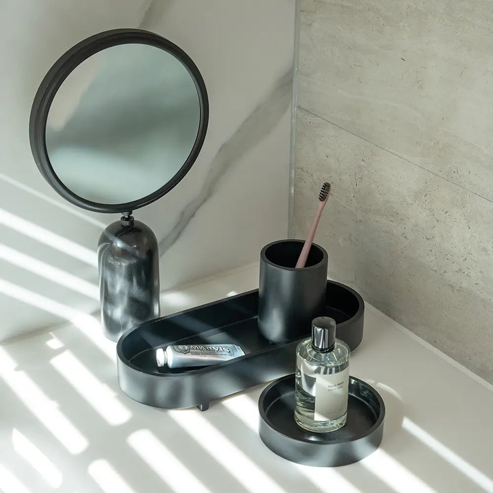Bathroom setup with a round mirror, toothbrush holder, and other toiletries on a tray.