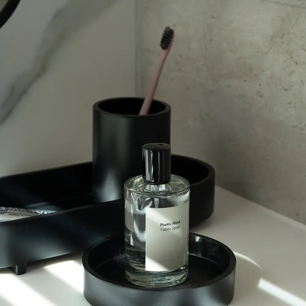 Bottle of perfume on a black tray with a toothbrush holder in the background.