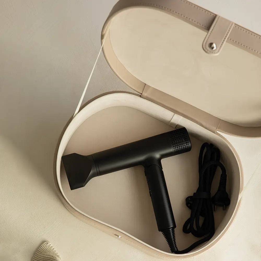 Black hair dryer in a beige storage case on a light brown surface