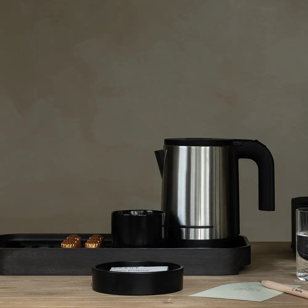 Black and silver electric kettle on a black tray on a wooden table with a neutral background