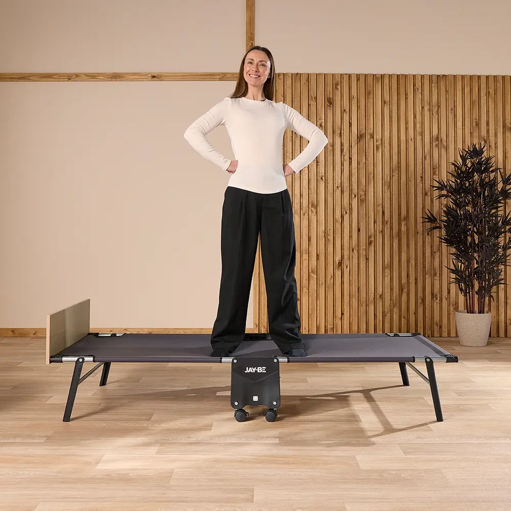 Woman standing on a bed in a room with wooden flooring and a plant.