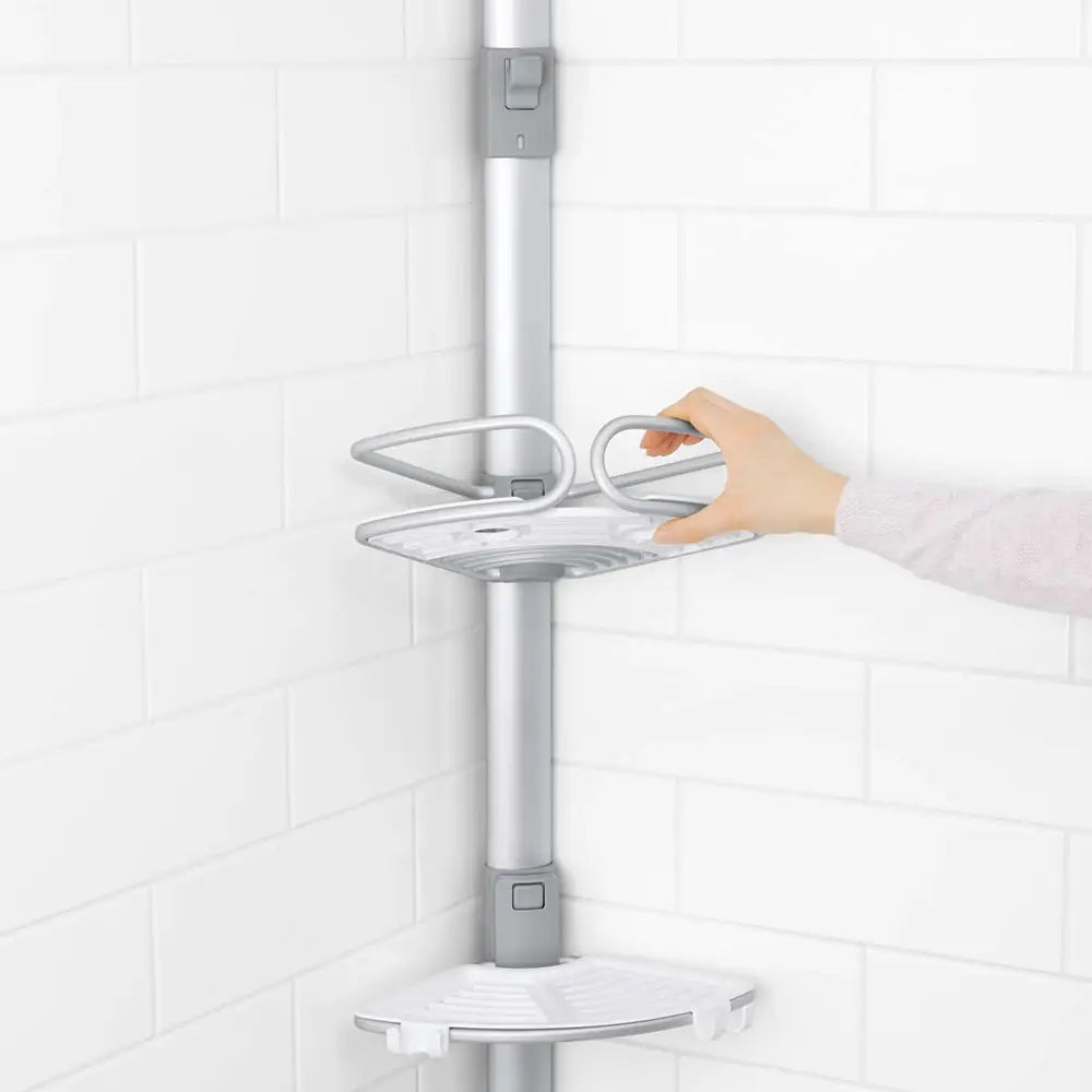 A silver and white shower shelf system mounted on a white tiled wall, with a hand adjusting the middle shelf.
