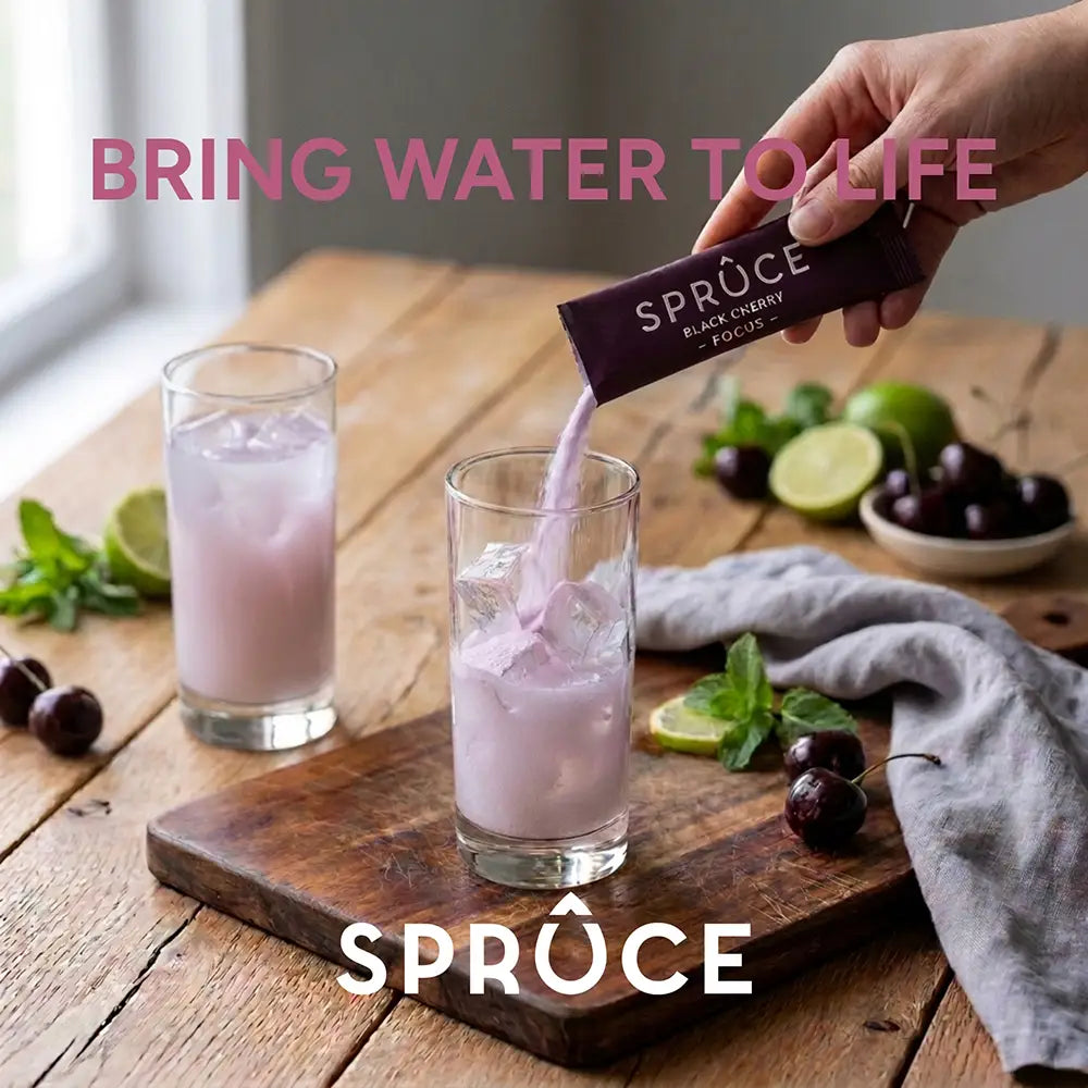 Hand pouring Spruce Black Cherry Focus sachet into a glass of iced water on a wooden board with cherries, 'Bring Water To Life' tagline