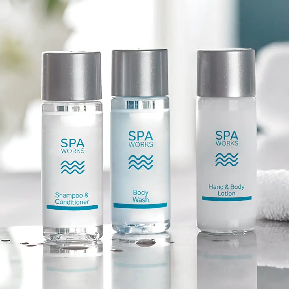 Three clear bottles of Spa Works products on a reflective surface with a blurred background.