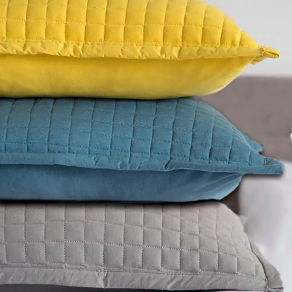 Stack of three crompton quilted pillows in yellow, blue, and gray on a neutral background