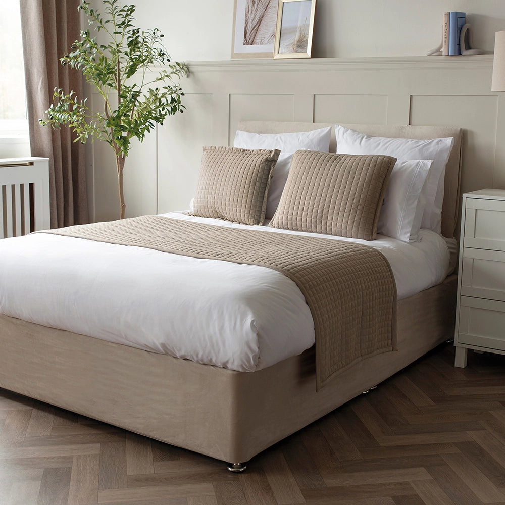 A gray Crompton runner on a bed with matching pillows and a vase of flowers on the side table.