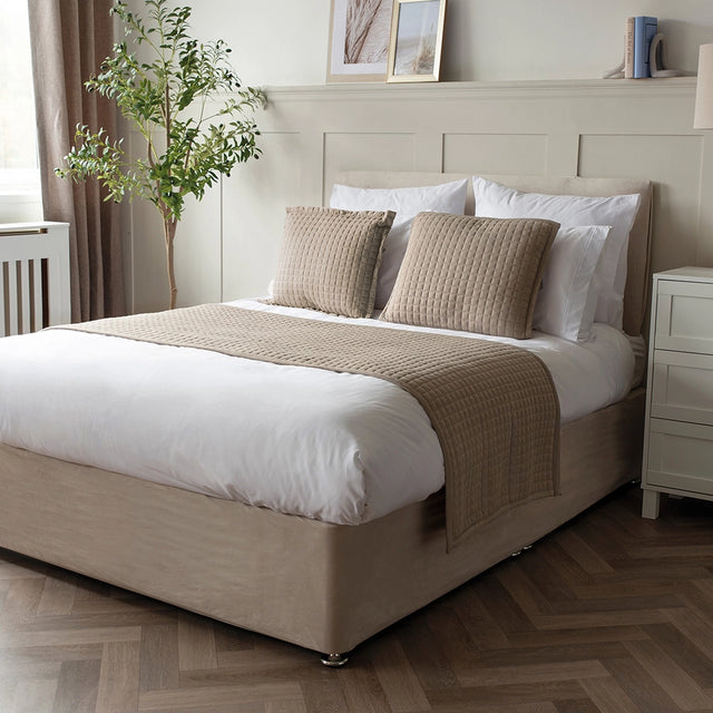 A gray Crompton runner on a bed with matching pillows and a vase of flowers on the side table.