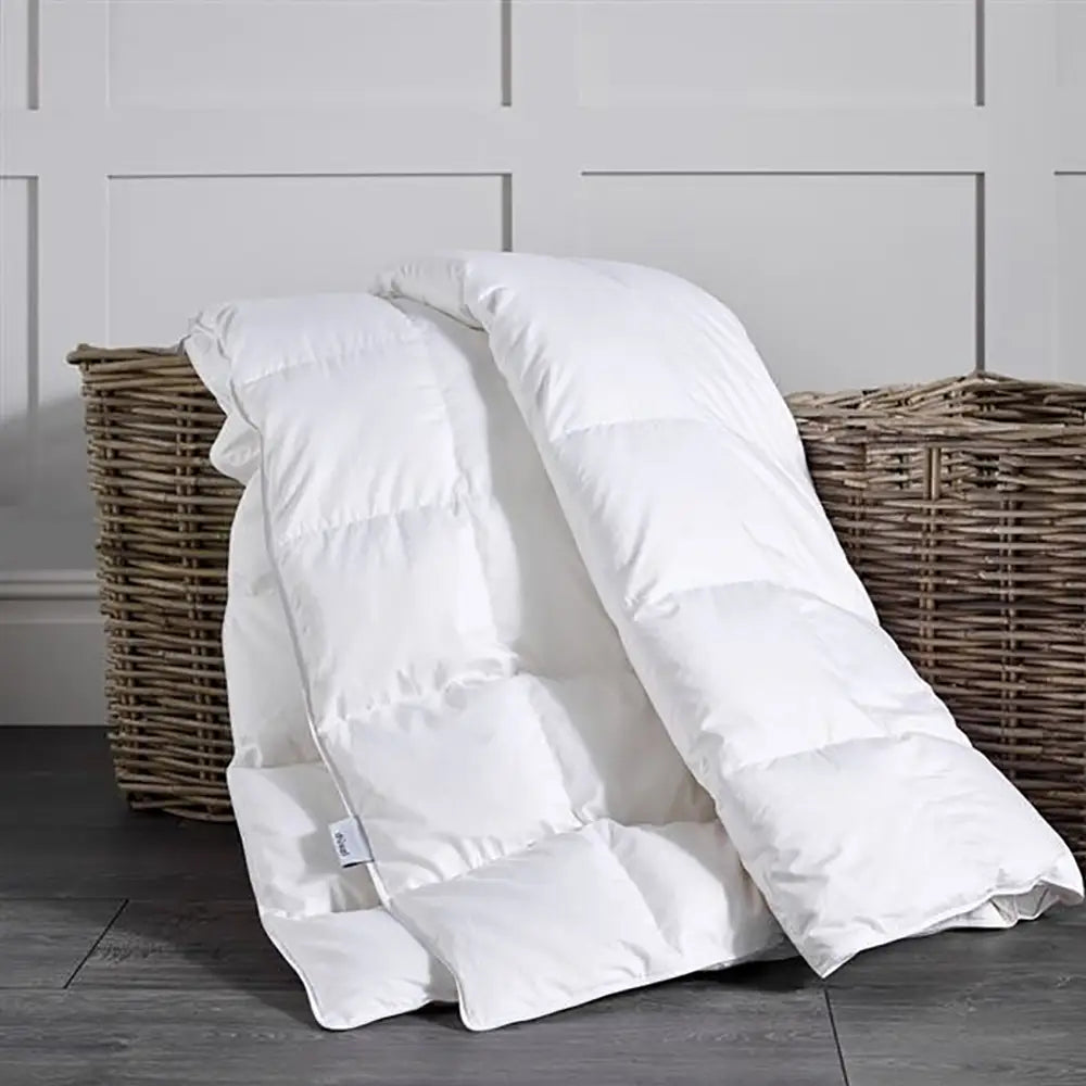 Luxury Goose Down Duvet draped over a wicker basket on a wooden floor with a light gray wall background.