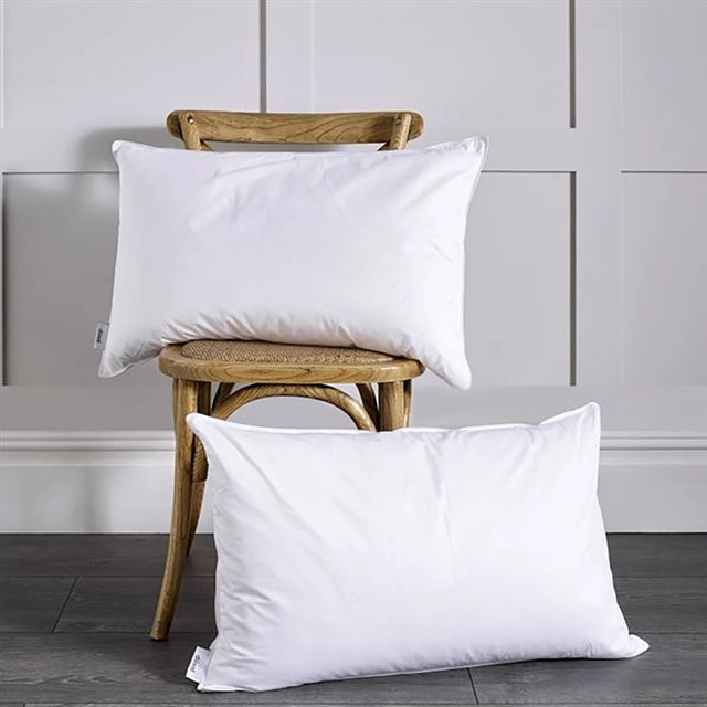 Two white pillows with a piped edge, placed on a wooden stool against a white background.