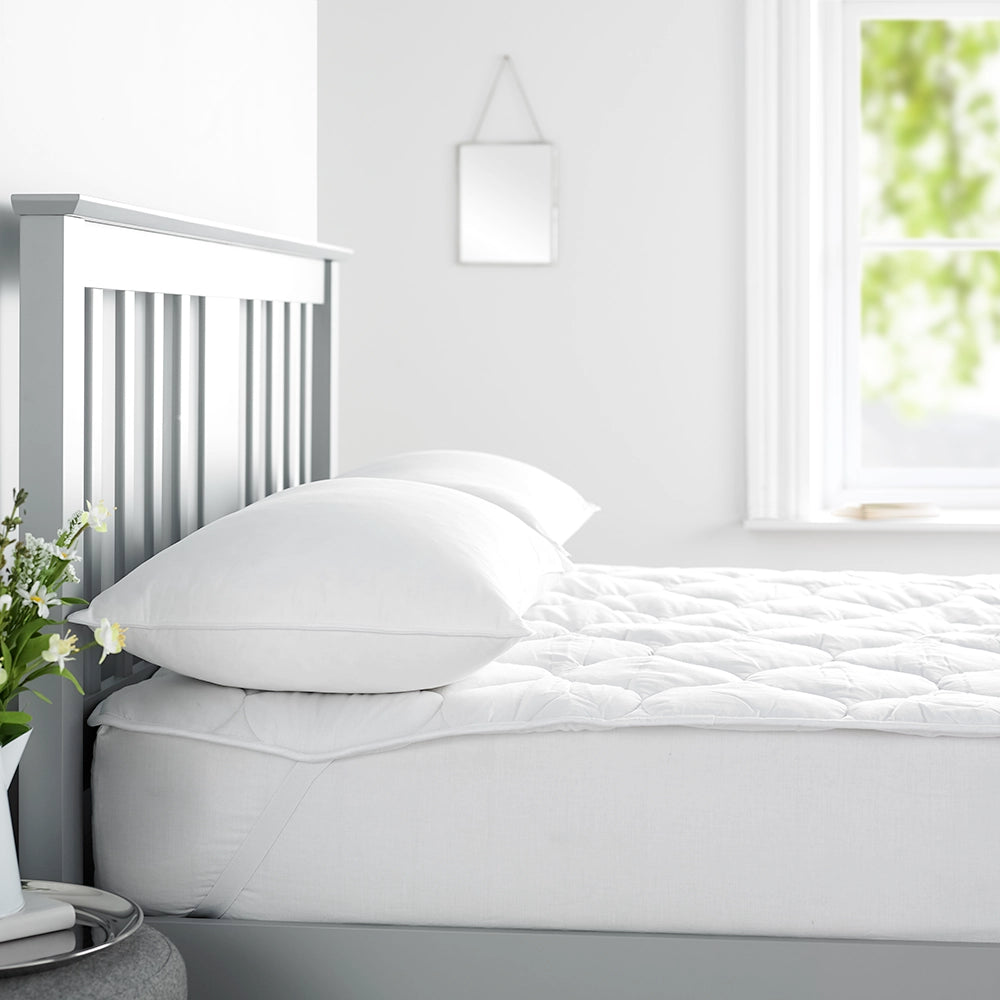 Image of bed with quilted mattress comforter showing elastic straps at the corner