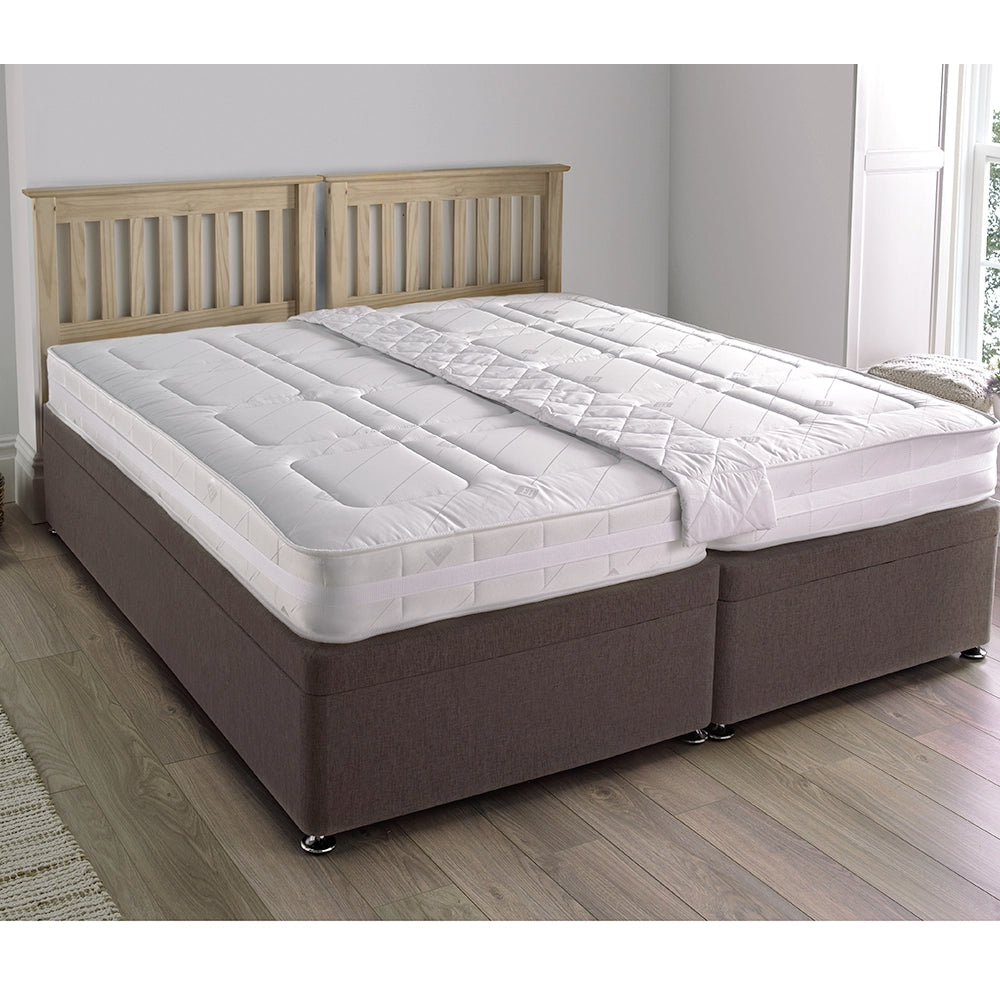 Two single beds linked together with a quick link belt to form a super king size bed, with a white quilted pad on top.