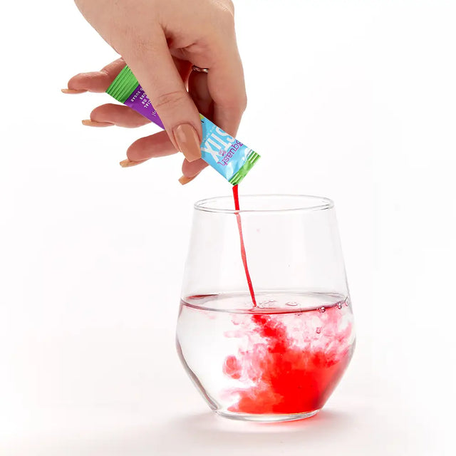 Hand pouring Apple and Blackcurrant Stix liquid from a packet into a glass on a white background