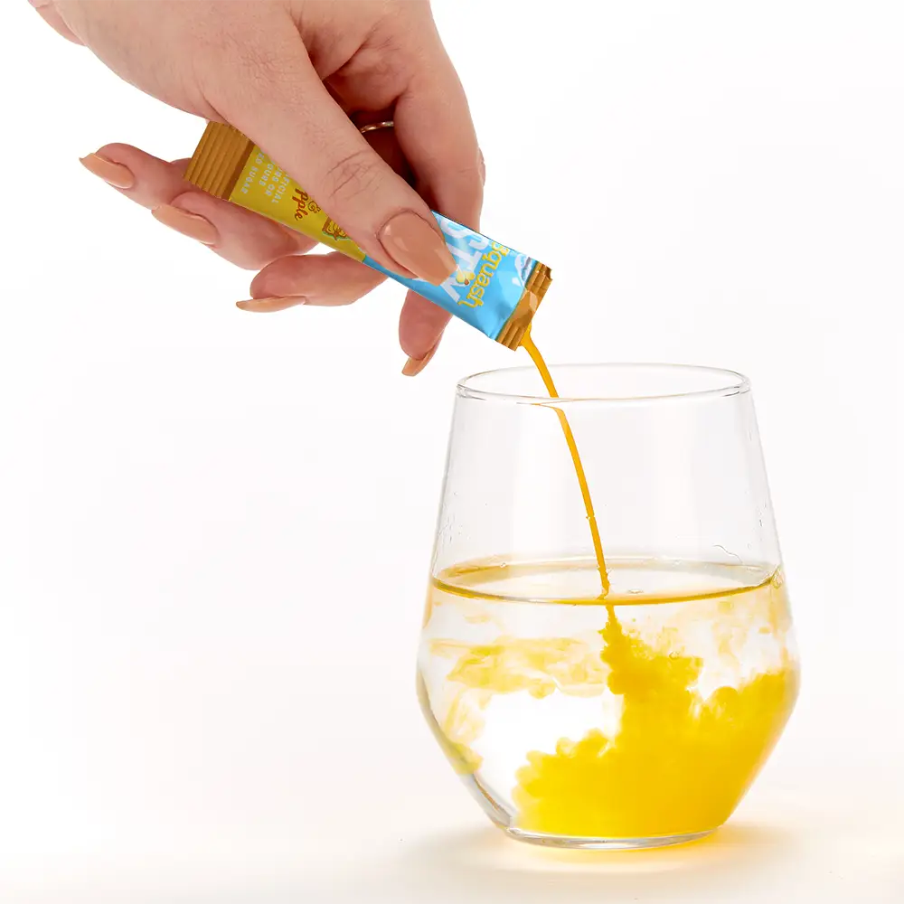 Hand pouring Orange & Pineapple Stix liquid from a packet into a glass on a white background