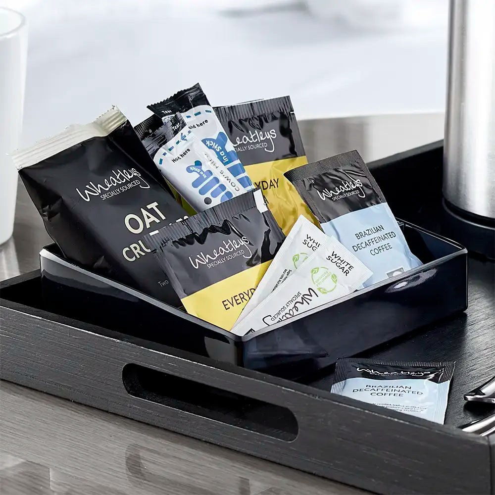 Collection of coffee and tea packets in a black tray on a wooden surface.