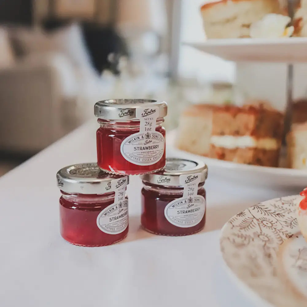 Three jars of strawberry jam on a table with a blurred background of pastries and cake