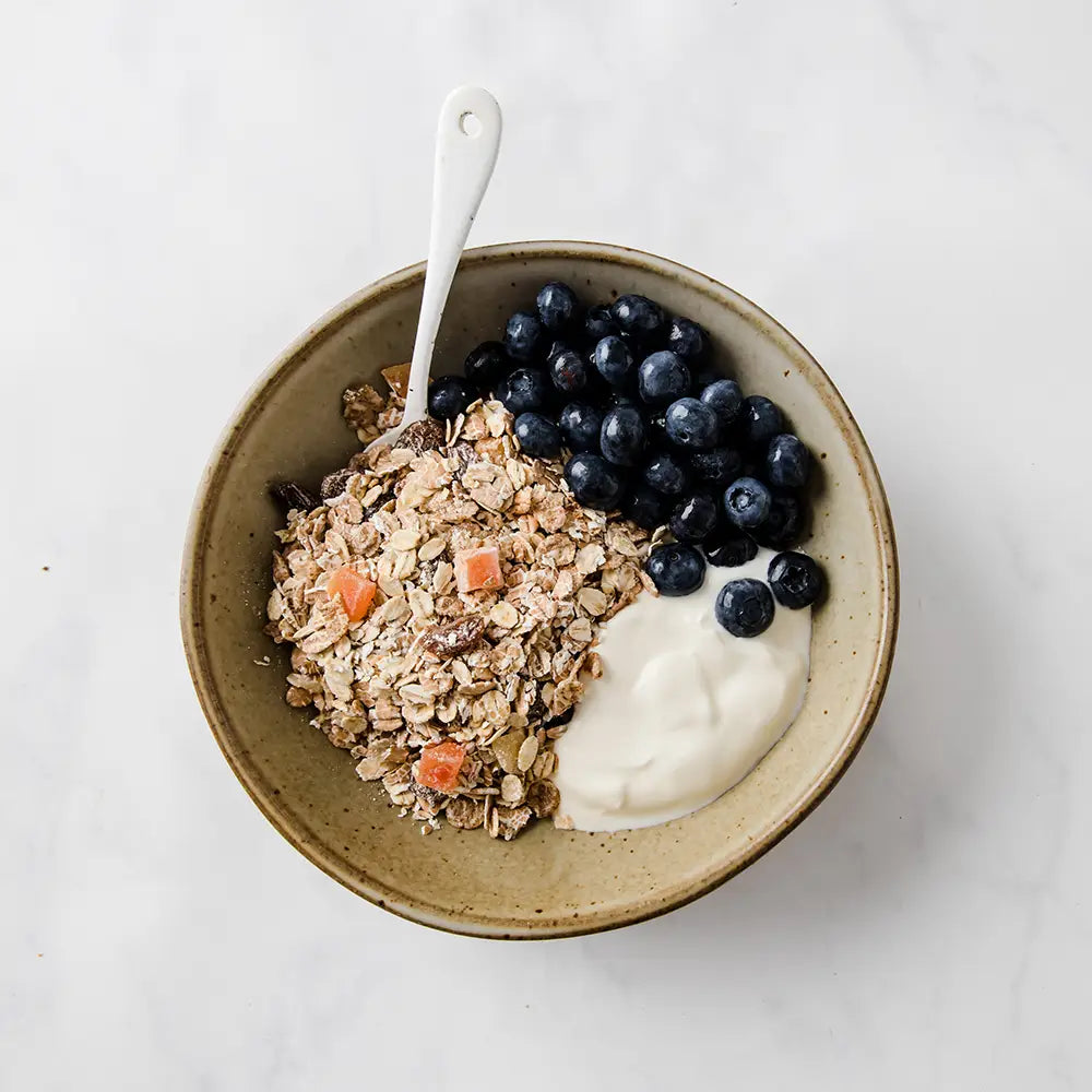 Bowl of Dorset Cereals Simply Fruity Muesli with yogurt and blueberries on a white background