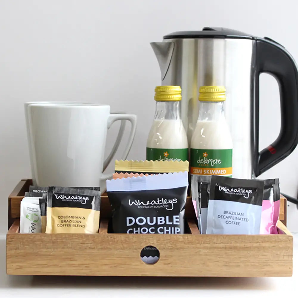 Coffee-making set with a kettle, mug, and coffee packaging on a wooden tray.