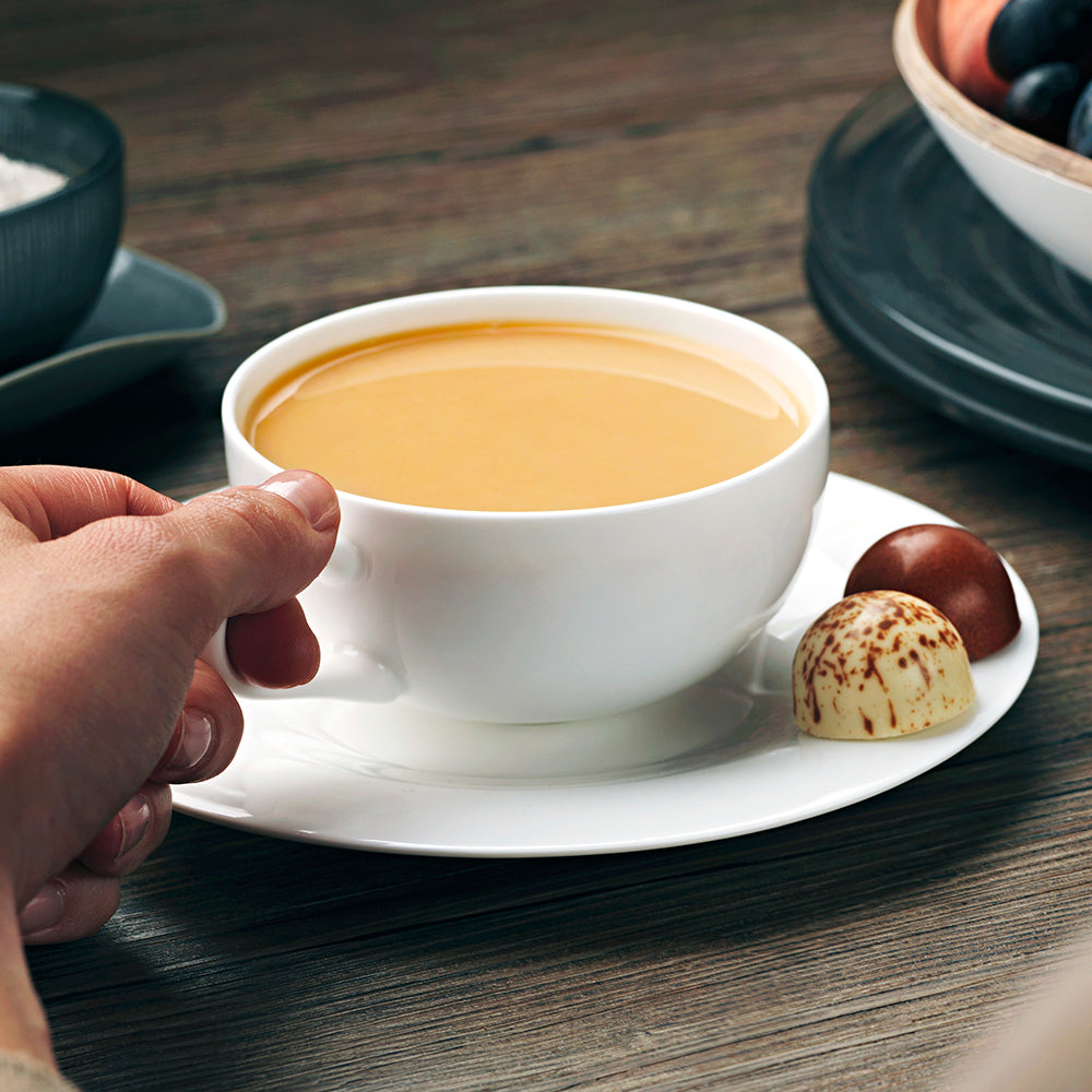 A cup of Birchall Great Rift Breakfast Tea served with milk in a white tea cup served with two fine chocolates on the saucer.