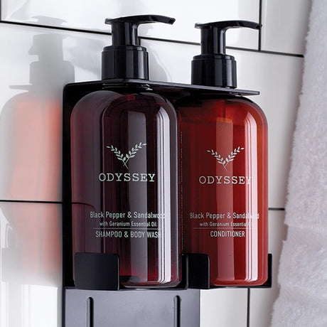 Two bottles of Odyssey shampoo and conditioner on a black brackets against a tiled bathroom wall.