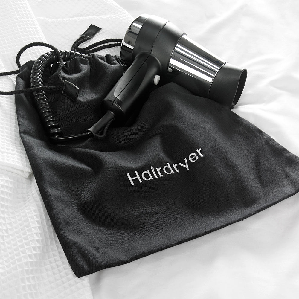 Black embroidered hairdryer bag on a bed with a hair dryer