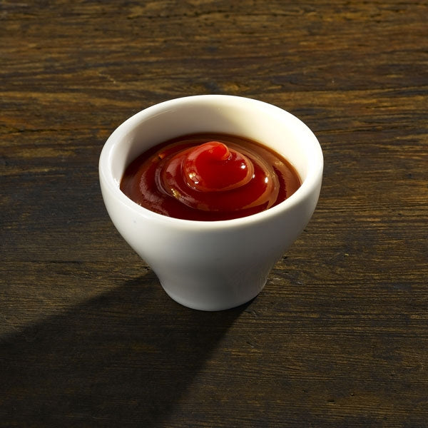 High performance toughened porcelain white porcelain bowl containing a swirl of red sauce, placed on a wooden surface.