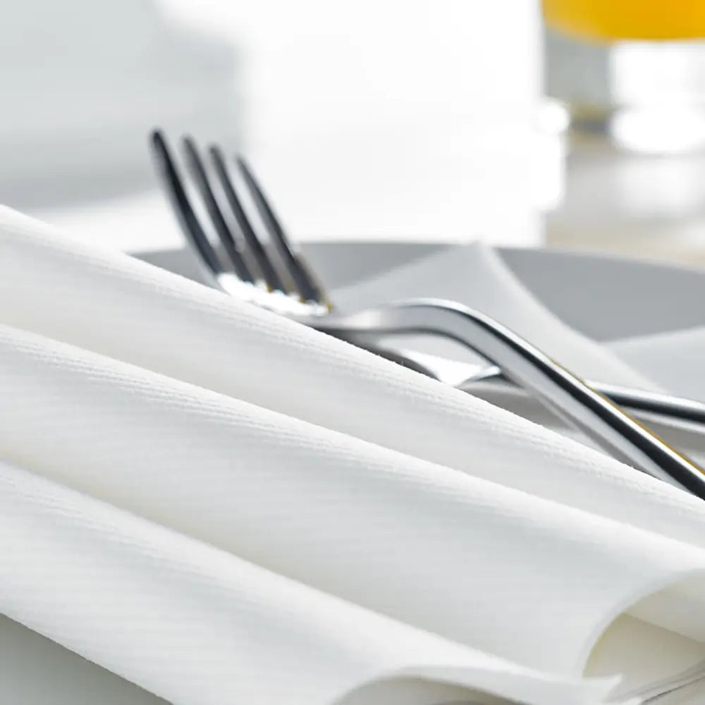Close-up of Airlaid white napkins with silverware on a white plate with a blurred background