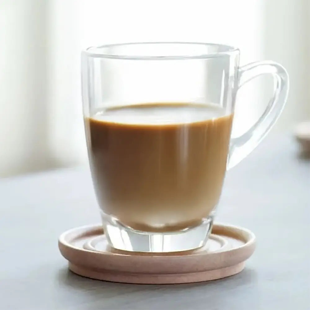 Clear glass mug with a tea on a light wooden coaster, blurred background