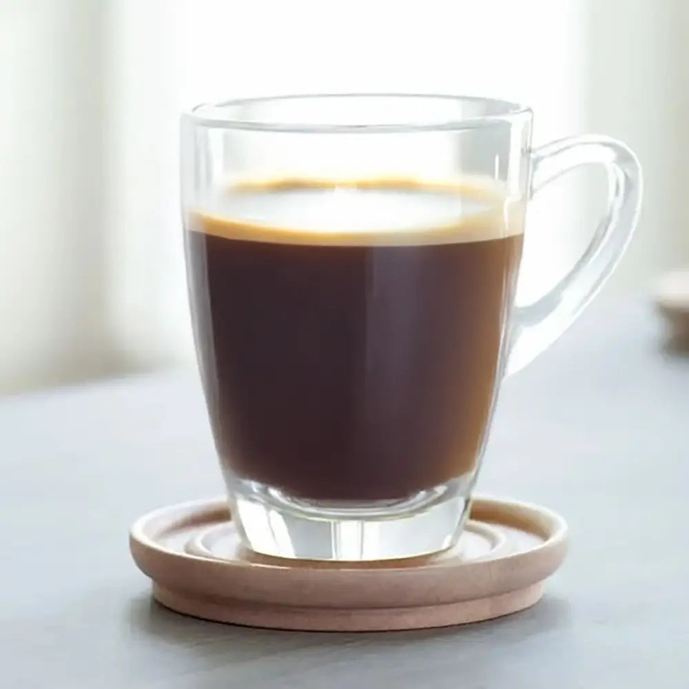 Clear glass mug with a wooden coaster on a light surface
