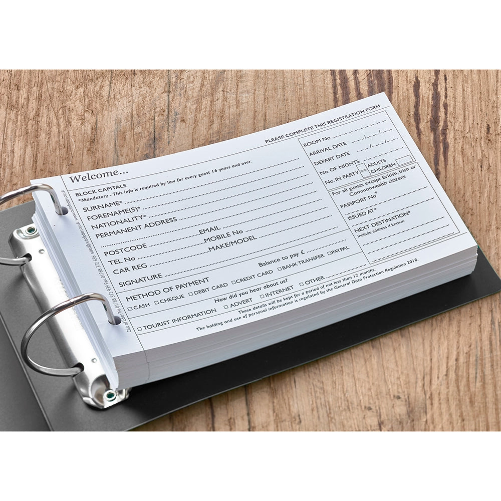 A welcome guest registration card with printed fields for personal information in a black plastic ring bound folder, lying on a wooden surface.