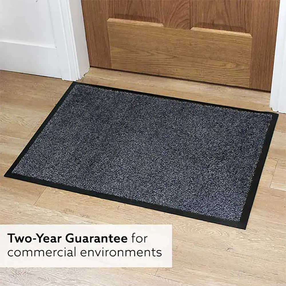 A rectangular, dark gray washable entrance door mat made of nylon with a rubber base, placed on a wooden floor with a two-year guarantee text overlay.