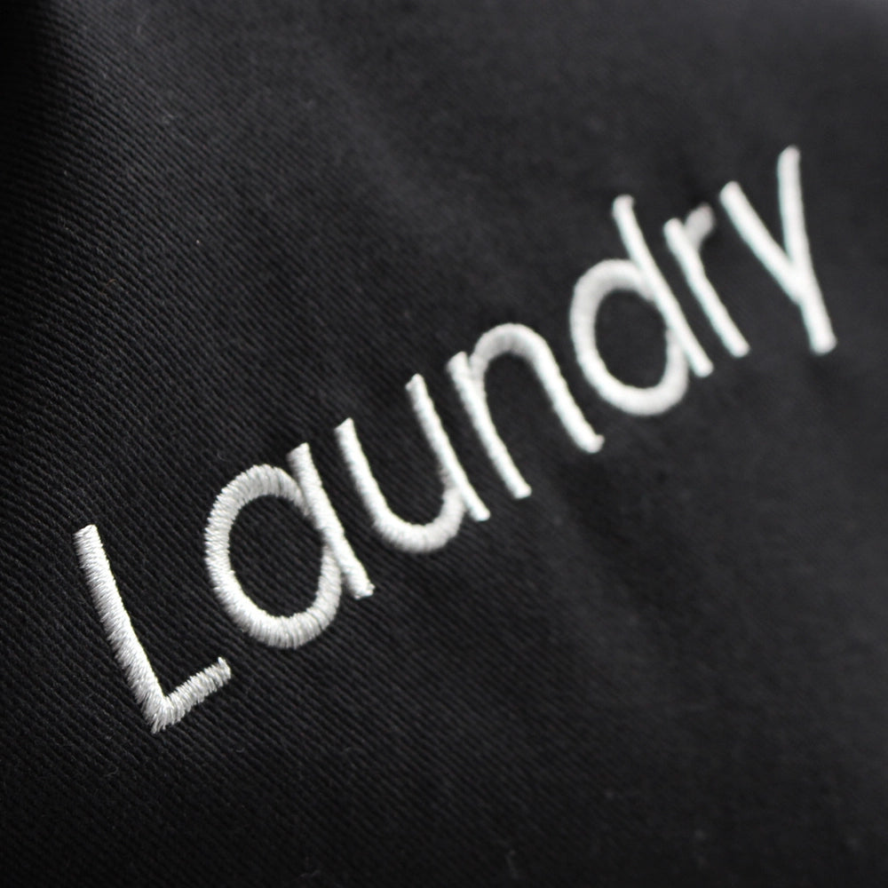 Close up of word "Laundry" embroidered in white thread on the side of the black laundry bag