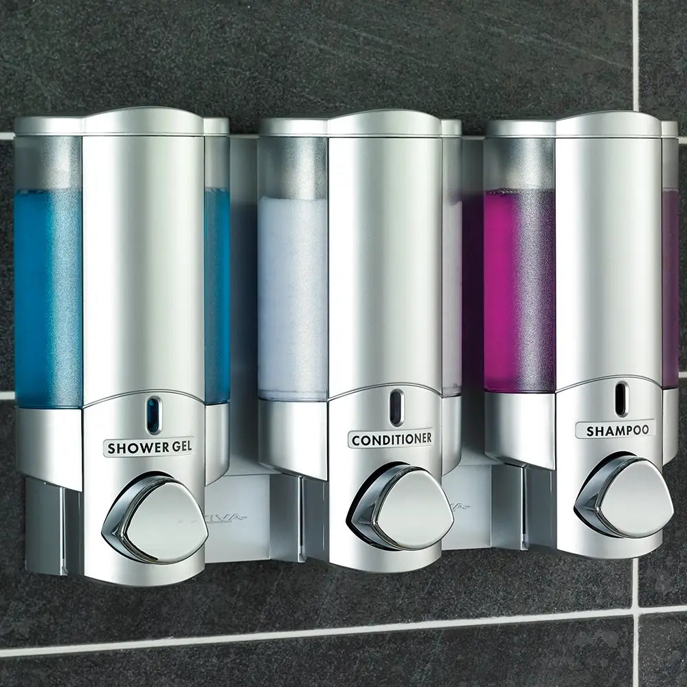 Aviva Triple Soap Dispenser - Three silver shower dispensers labeled 'Shower Gel', 'Conditioner', and 'Shampoo' on a tiled wall.