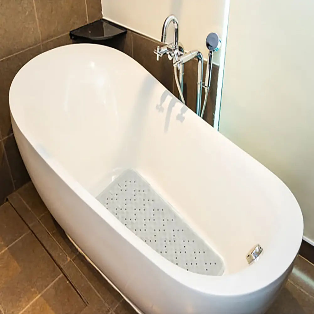 Non slip rubber bath mat in a white freestanding bathtub in a bathroom setting with tiled walls and a glass shower door.