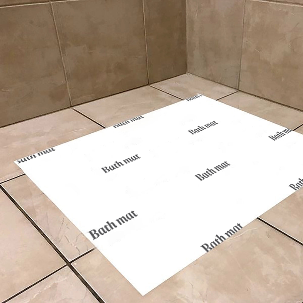 A disposable paper bath mat with the words 'Bath mat' printed in black onto the white surface, placed on a tiled bathroom floor.