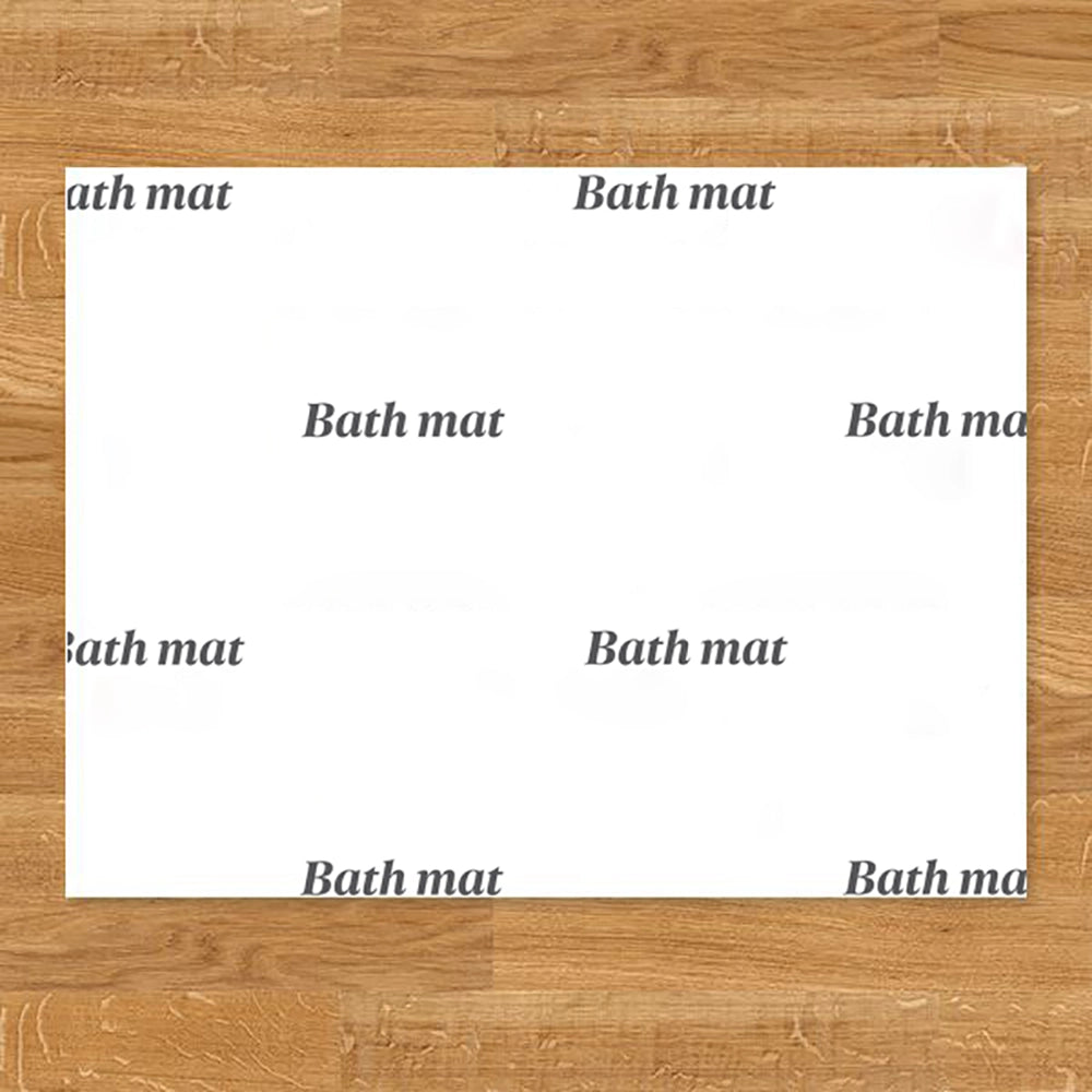 A disposable paper bath mat with the words 'Bath mat' printed in black onto the white surface, placed on a wooden floor
