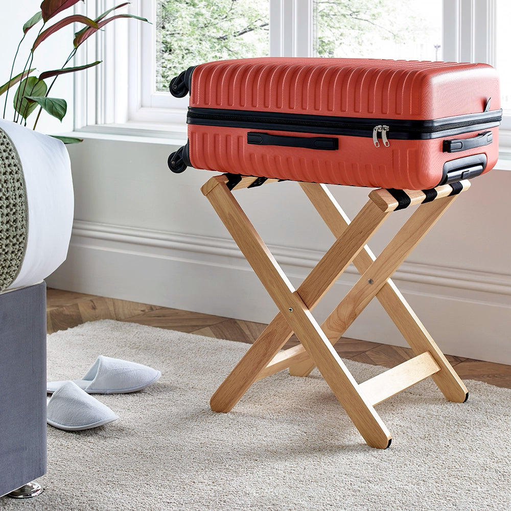Pale wood luggage stand holding an Orange suitcase in a bedroom setting
