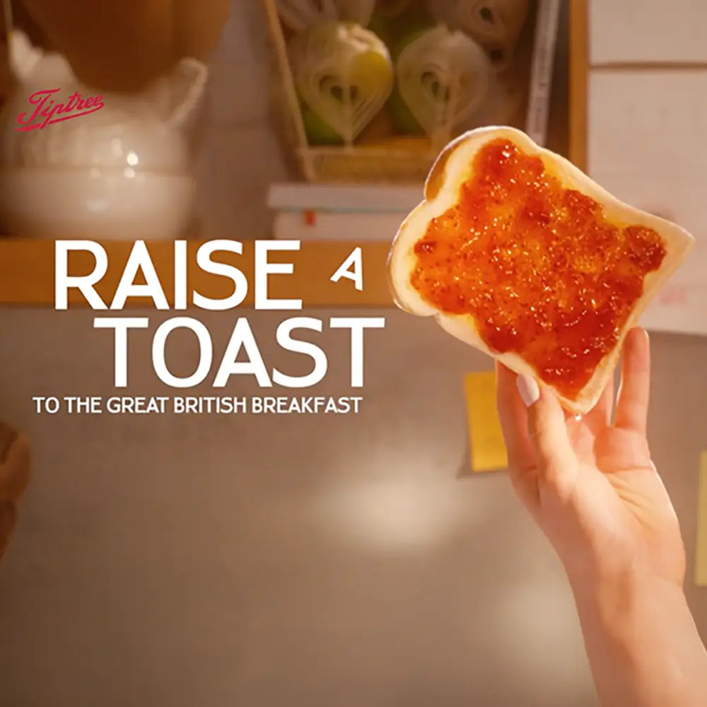 Hand holding a piece of toast with jam, with 'Tiptree' branding and text 'Raise a Toast to the Great British Breakfast'.