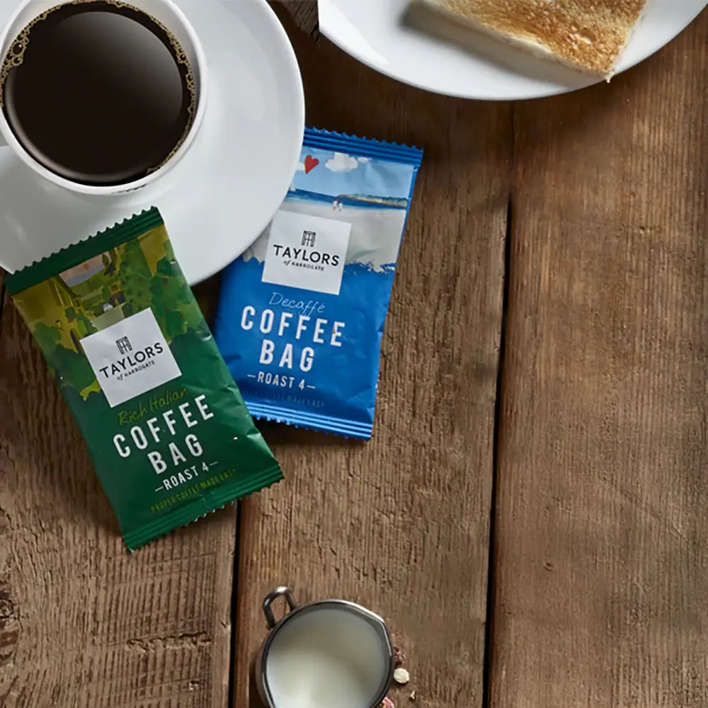 Two coffee bags from Taylors on a wooden surface with a cup of coffee and toast.