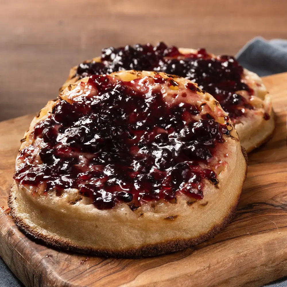Two crumpets with jam on a wooden cutting board