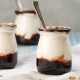 Three small glass jars filled with jam and yoghurt layered on a textured surface.